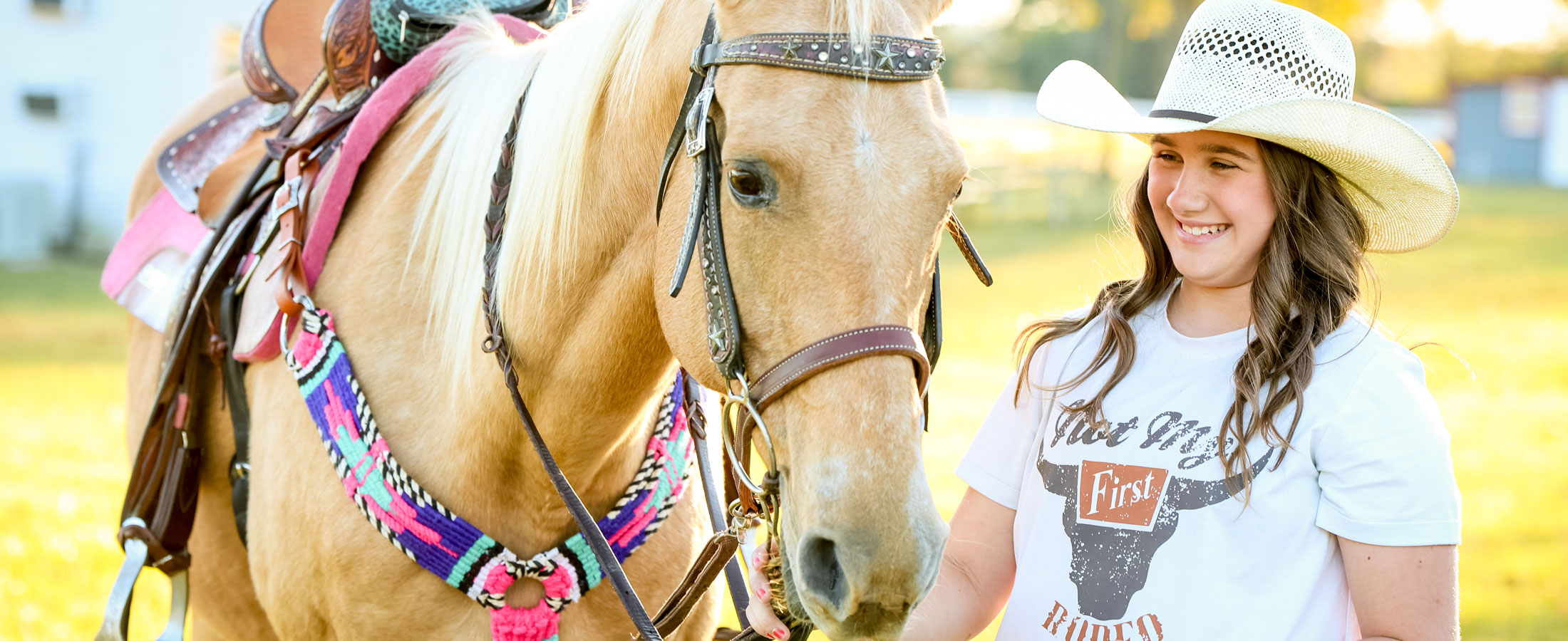 Ella Nipper standing next to her palomino horse, wearing a straw cowboy hat and smiling.